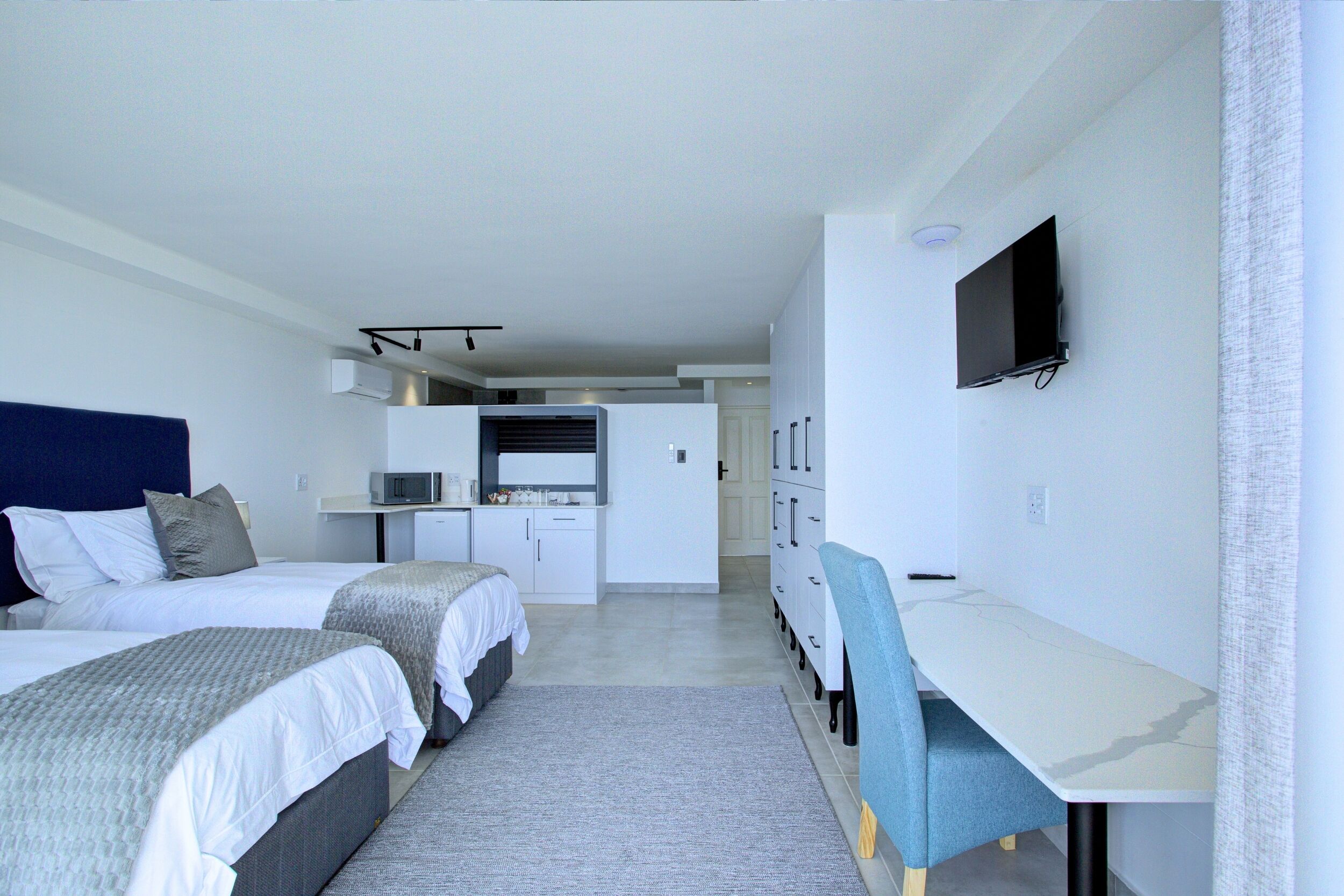 Una habitación de hotel con dos camas, un escritorio, un televisor y una kitchenette.