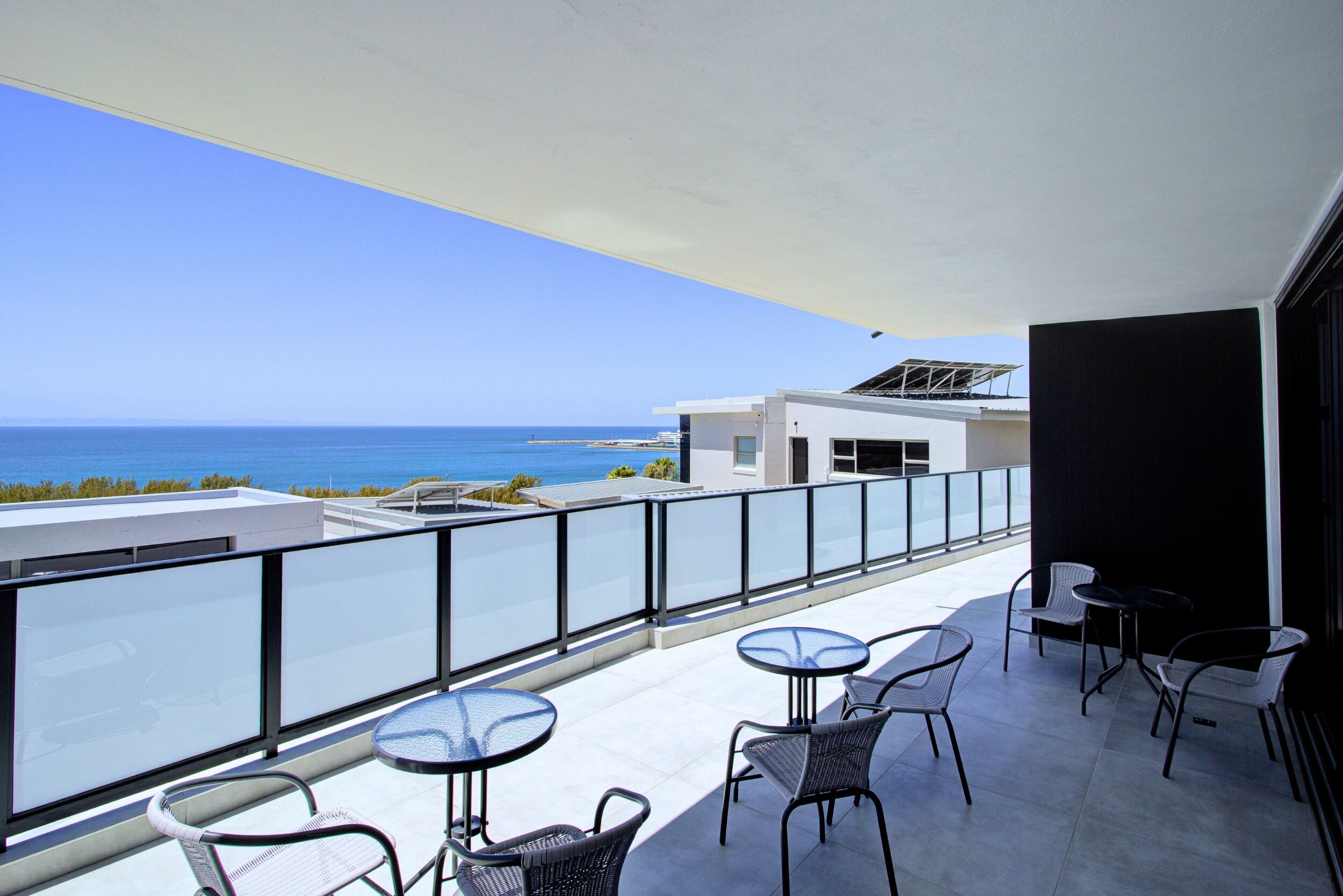 Een balkon met een helder uitzicht op zee, voorzien van tafels en stoelen.