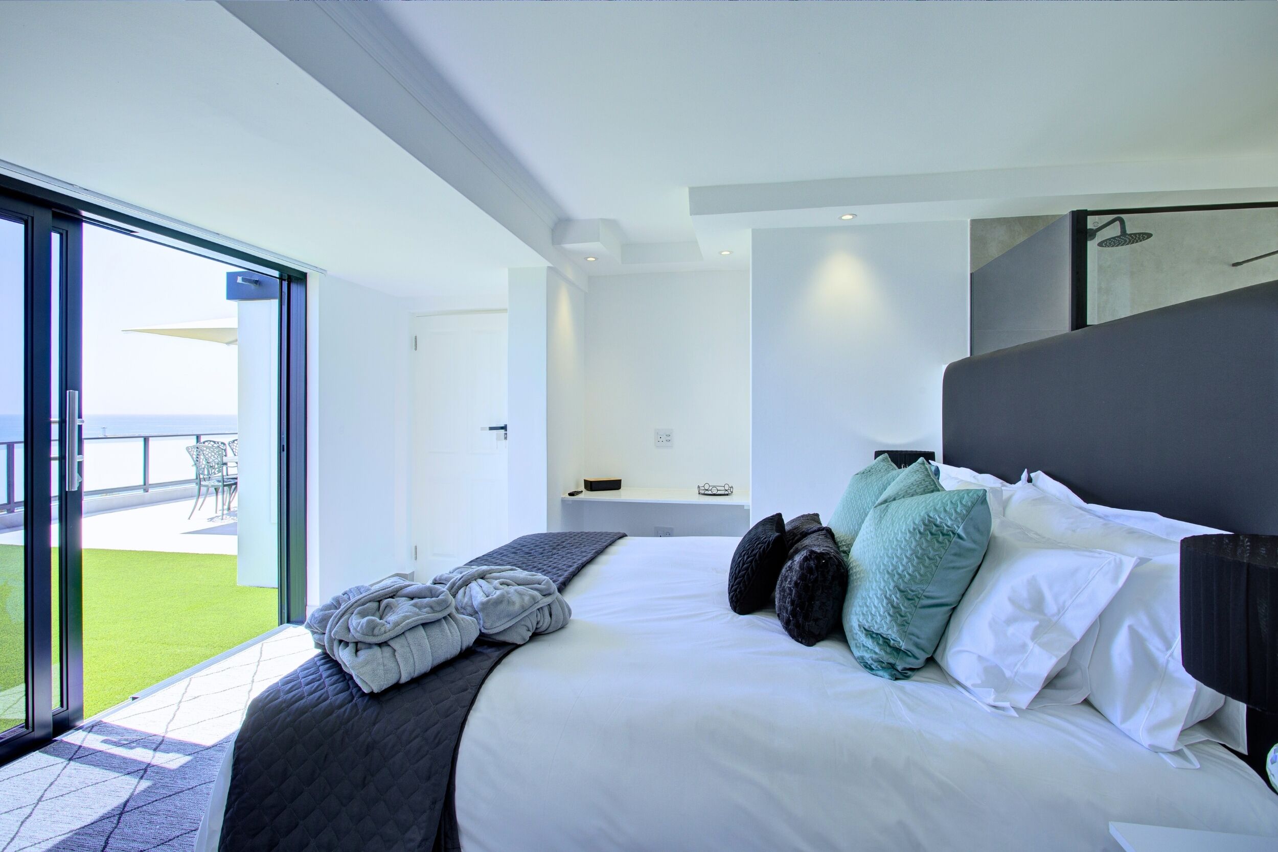 A modern bedroom with a large bed, a view of a green outdoor area, and a sliding door leading to a balcony.