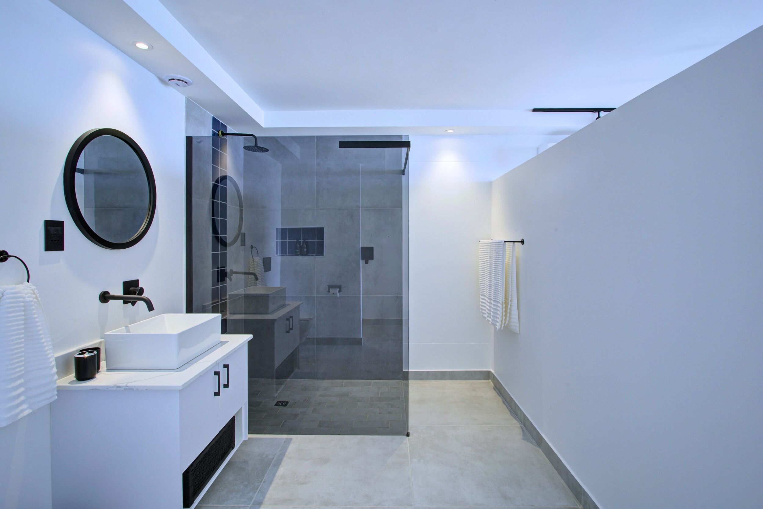 A modern bathroom with a white vanity, a round mirror, and a glass-enclosed shower.