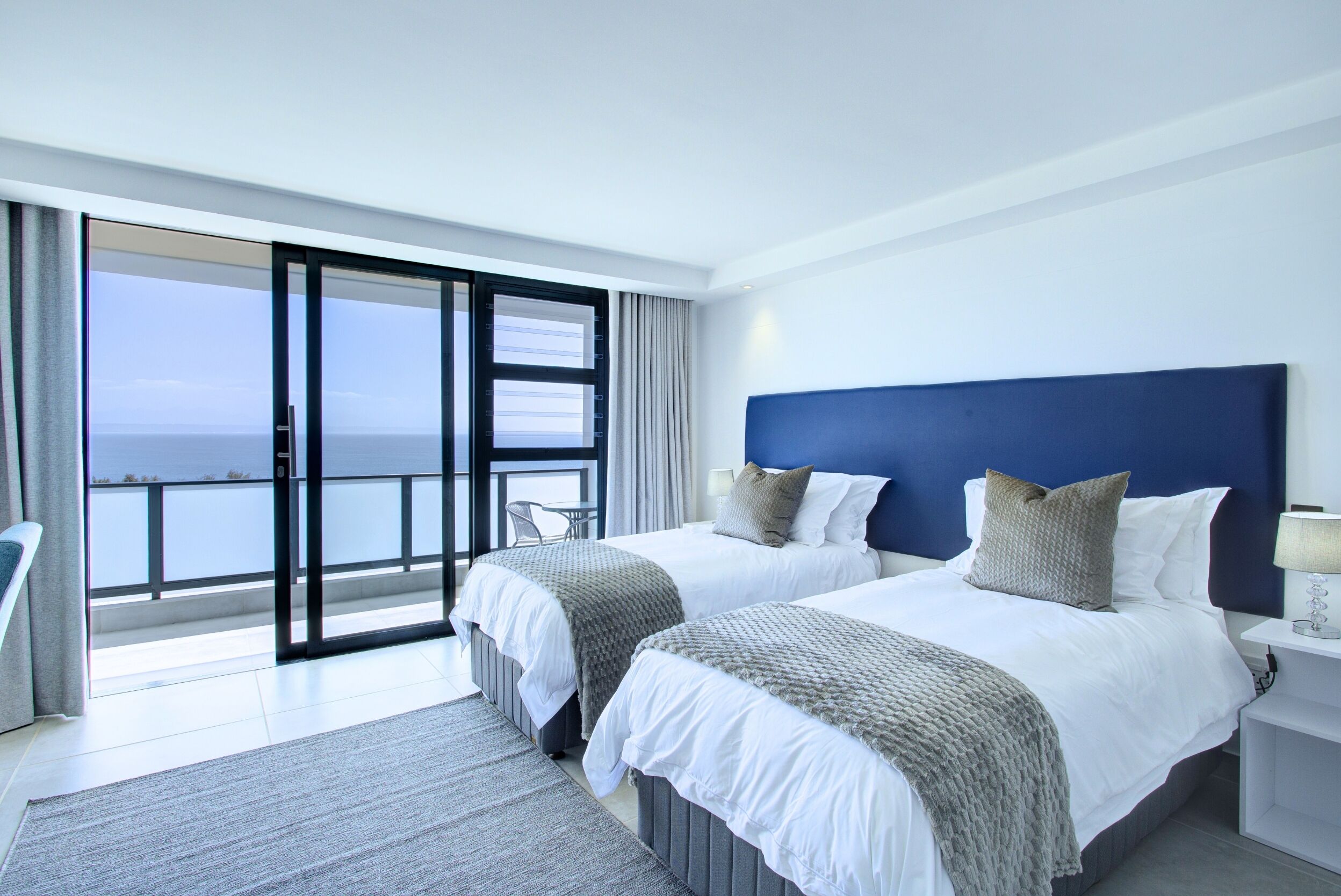 Habitació d'hotel amb dos llits, un balcó amb vista al mar i un disseny modern.