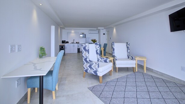 A modern living room with a dining table, two patterned armchairs, a small side table, and a grey rug. - Mosselbay Waterfront Accomodation  (Mossel Bay)