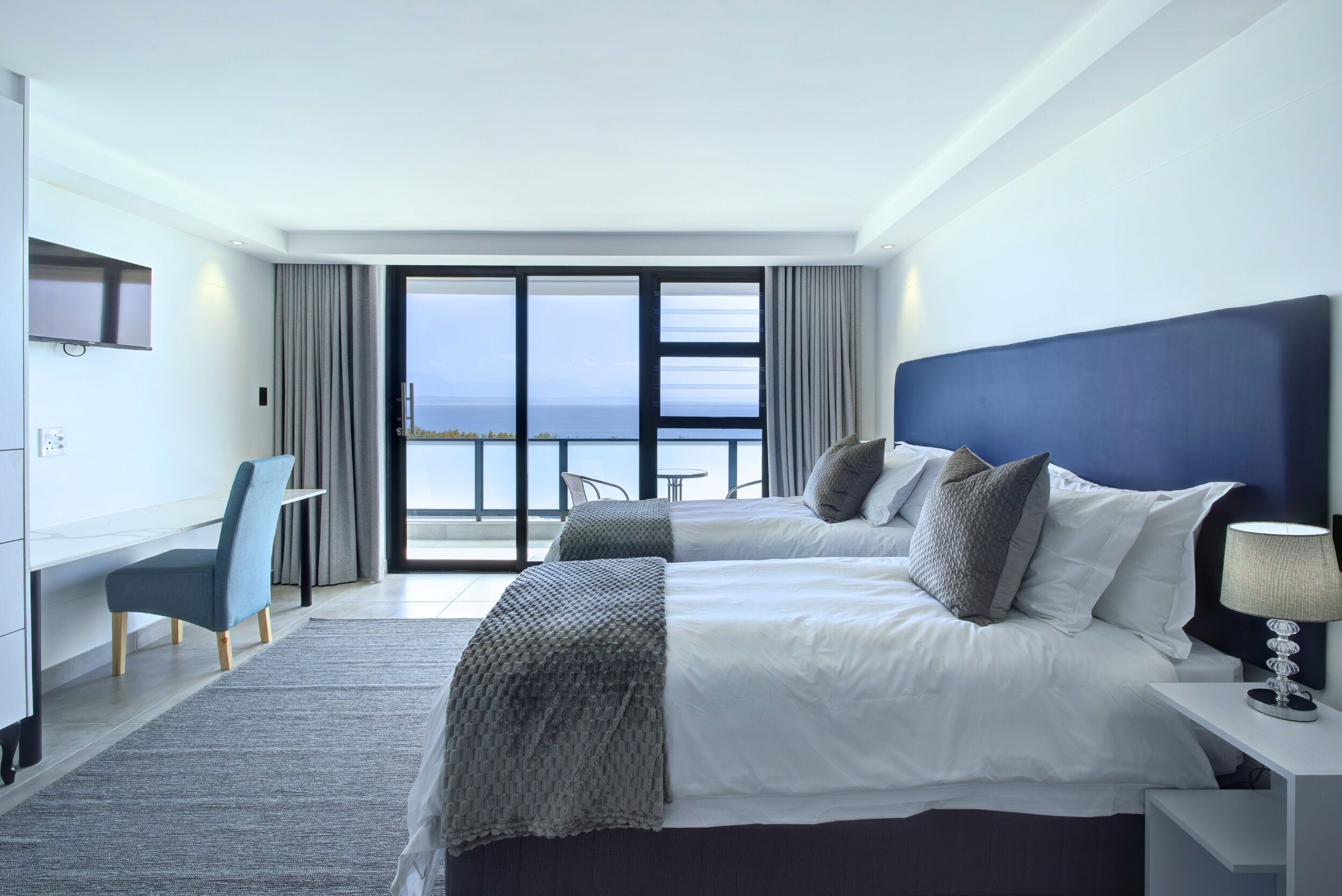 A modern hotel room with a large bed, a desk, and a view of the ocean.