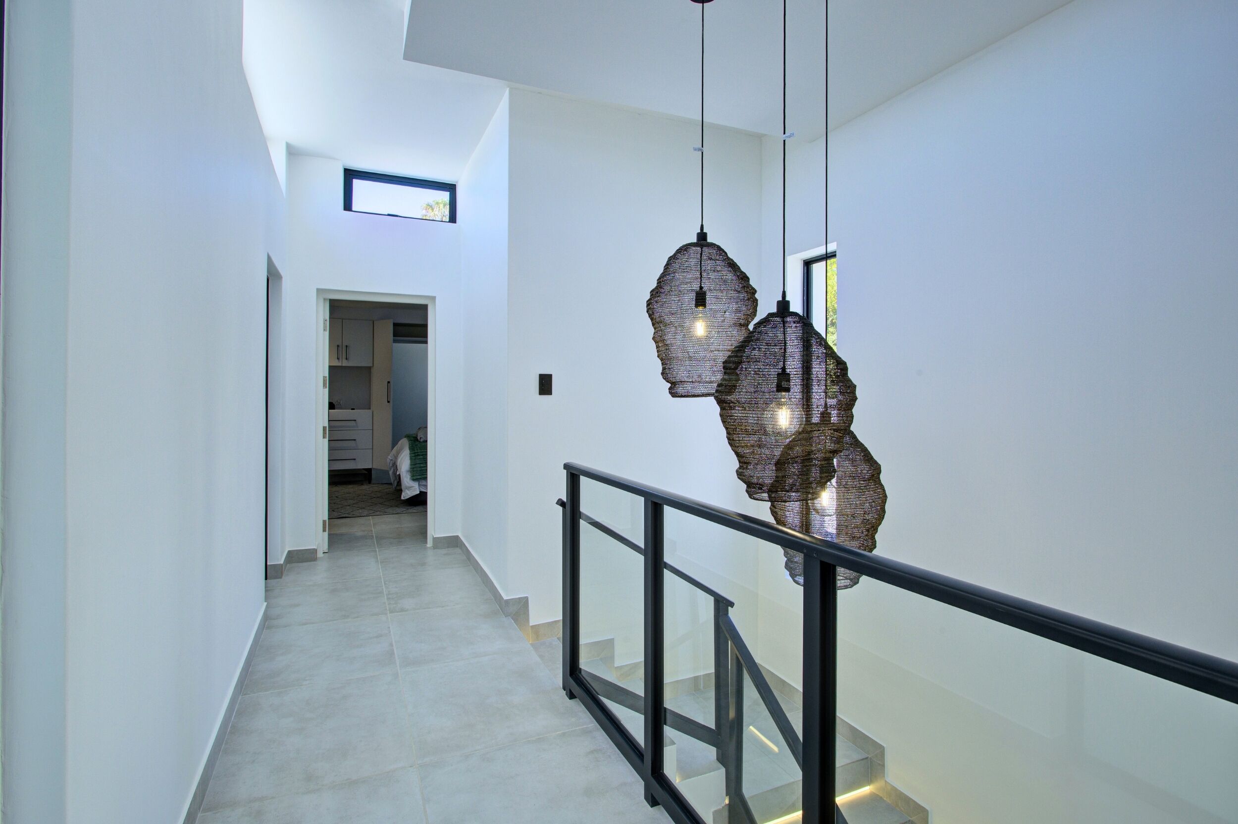 Ein modernes Interieur mit einer Treppe, einer Glastrennwand und hängenden Pendelleuchten.