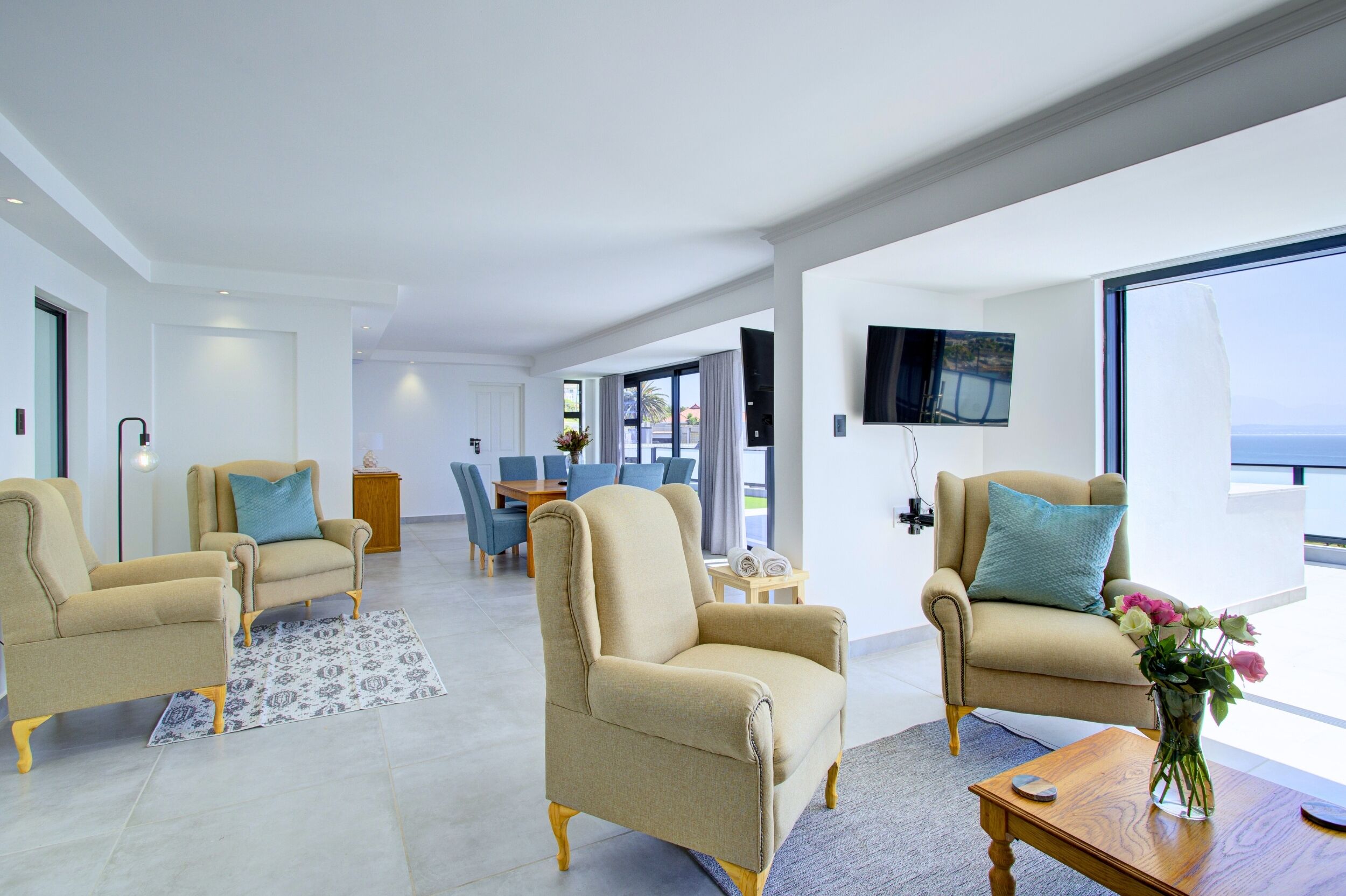 A modern living room with two beige armchairs, a wooden coffee table, and a vase with flowers.