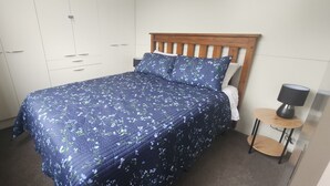 A bedroom with a bed, a wooden headboard, a bedside table with a lamp, and a wardrobe.