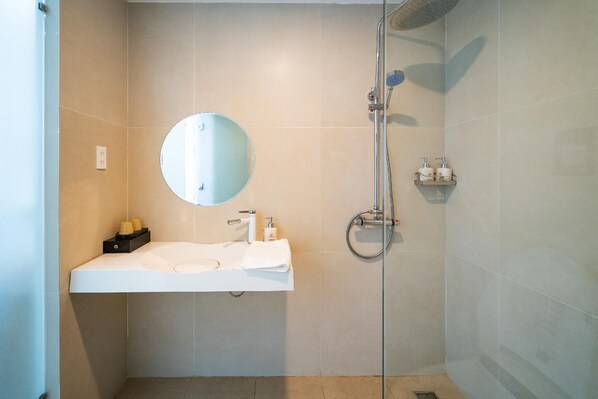 A modern bathroom with a white sink, a round mirror, a handheld showerhead, and a small shelf with toiletries. - Quy Nhon Sea Hotel (Quy Nhon Nam)