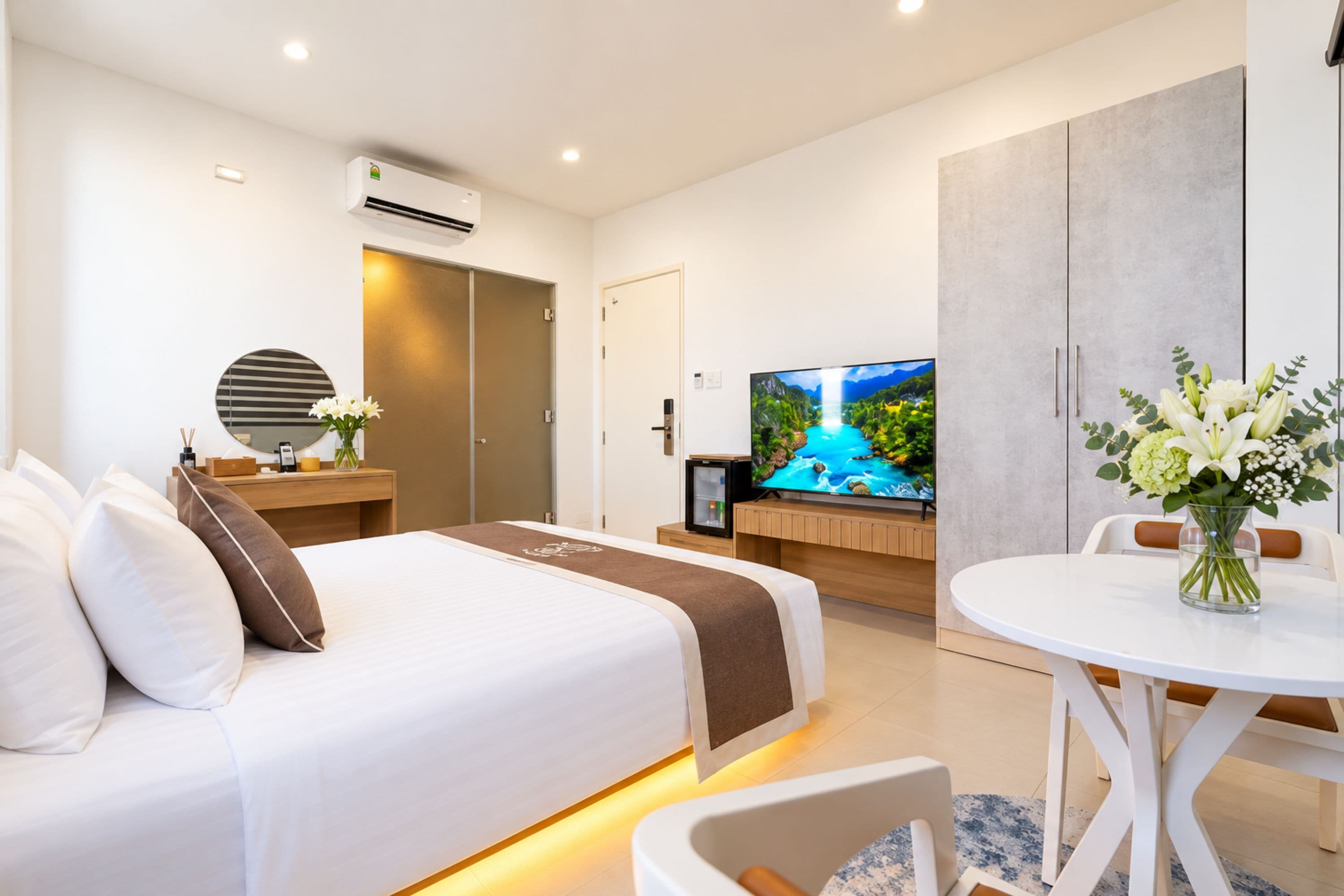 A modern hotel room with a bed, a TV, a desk, and a dining area.