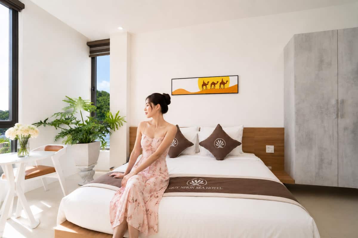 Una habitación de hotel moderna con una cama grande, vistas al exterior, un área de comedor y una planta en maceta.