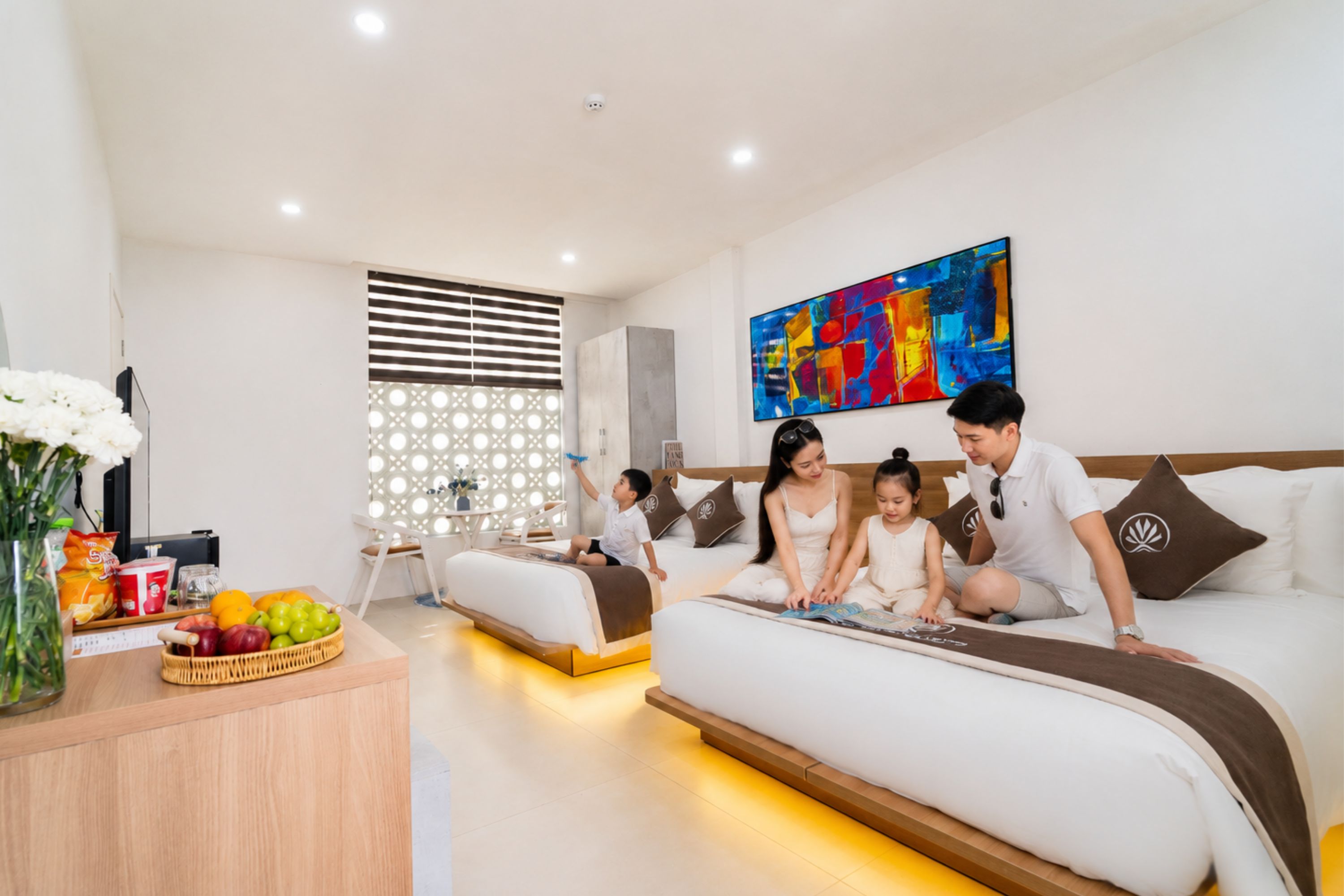 A modern hotel room with a large bed, a dining area, and a colorful abstract painting on the wall.