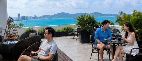 Una terraza con mobiliario de mimbre, una mesa con bebidas y vistas al mar y al horizonte de la ciudad.