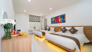A modern hotel room with a large bed, a desk with a fruit basket, and a colorful abstract painting on the wall.