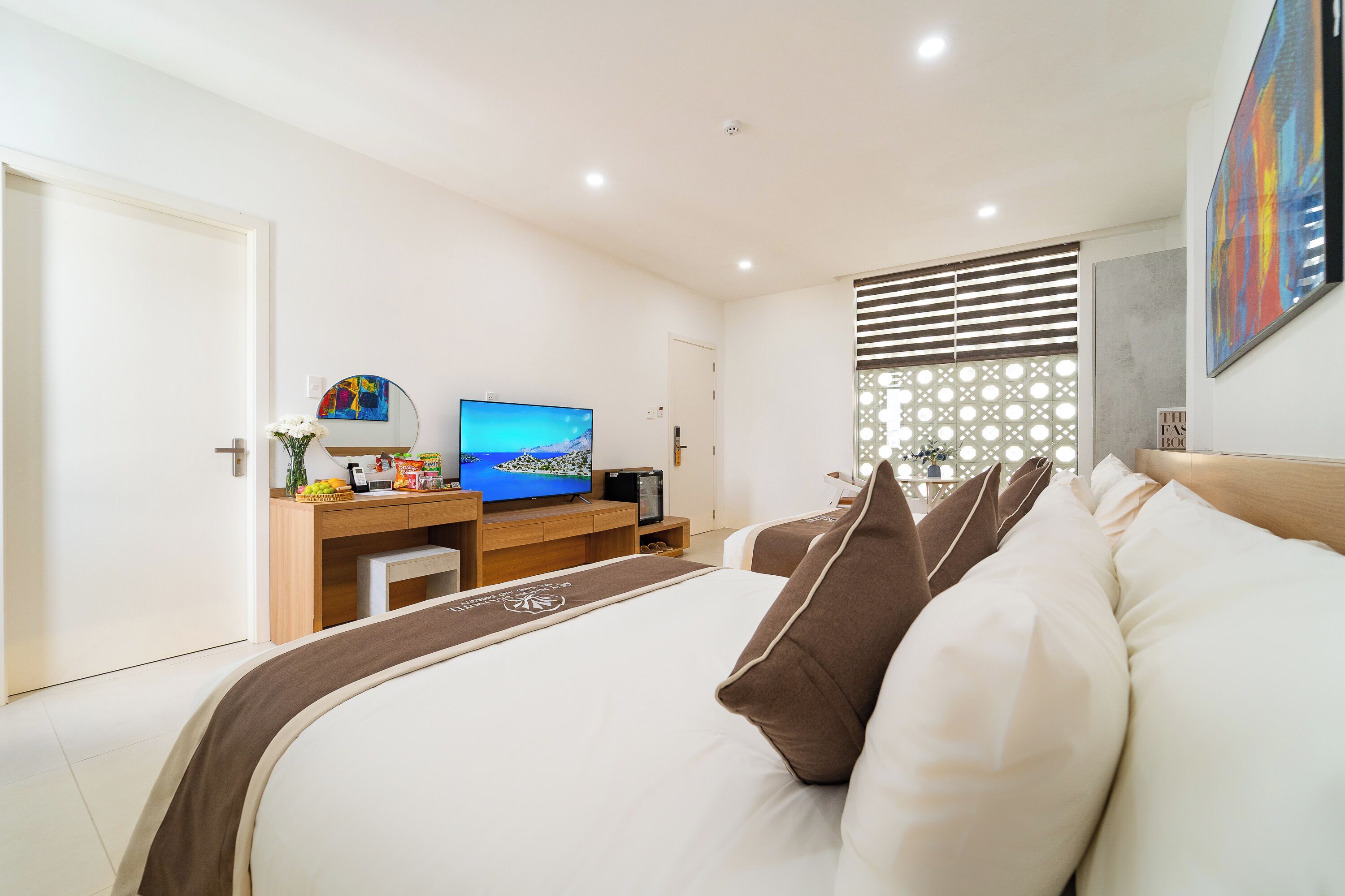 A hotel room with a large bed, a desk with a television, and a decorative wall.