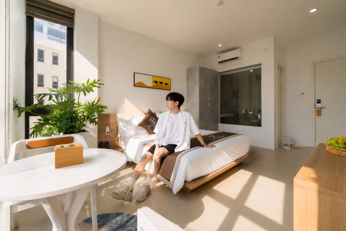 Una habitación de hotel moderna con cama, una mesa de comedor, una planta en maceta y un ventanal grande.