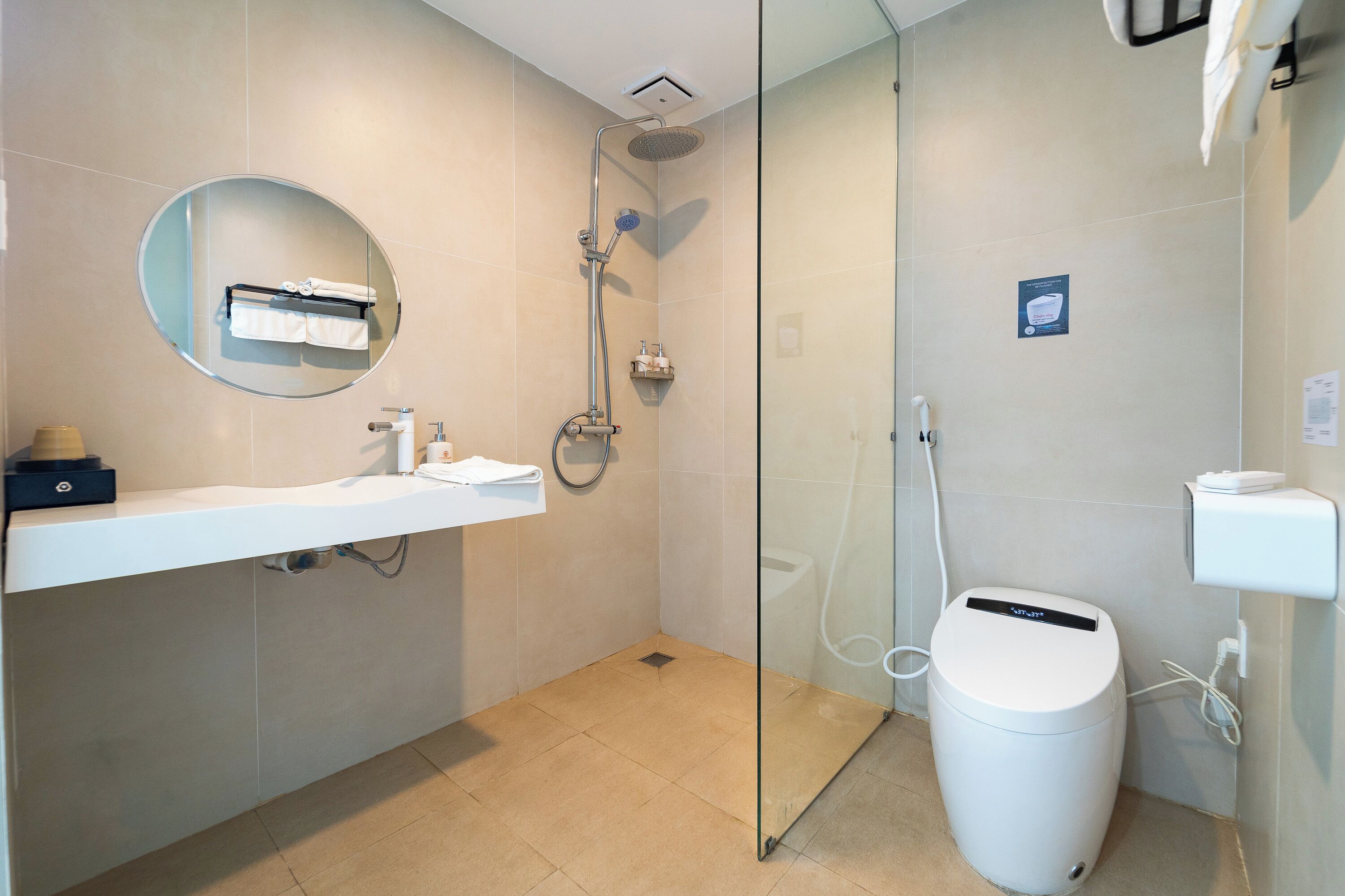 Une salle de bain moderne avec une douche à parois de verre, un miroir rond, un lavabo blanc et une poubelle.