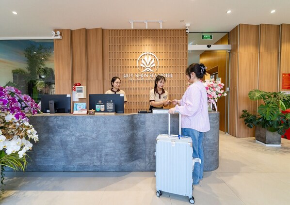 Un comptoir d’accueil d’hôtel avec un panneau en bois en arrière-plan, un écran numérique et un code QR.