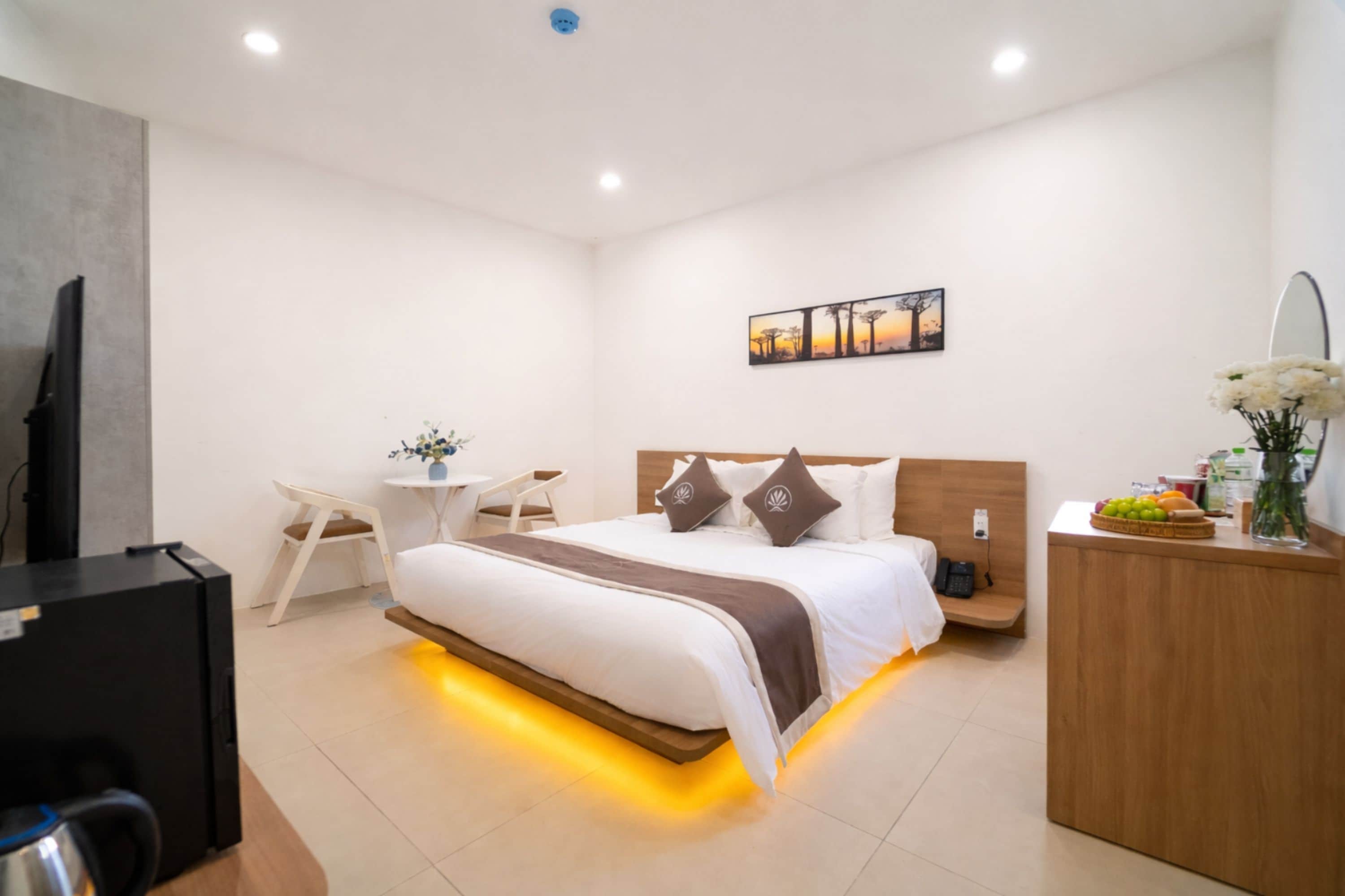 A modern hotel room with a bed, bedside table, chair, desk, and a television.