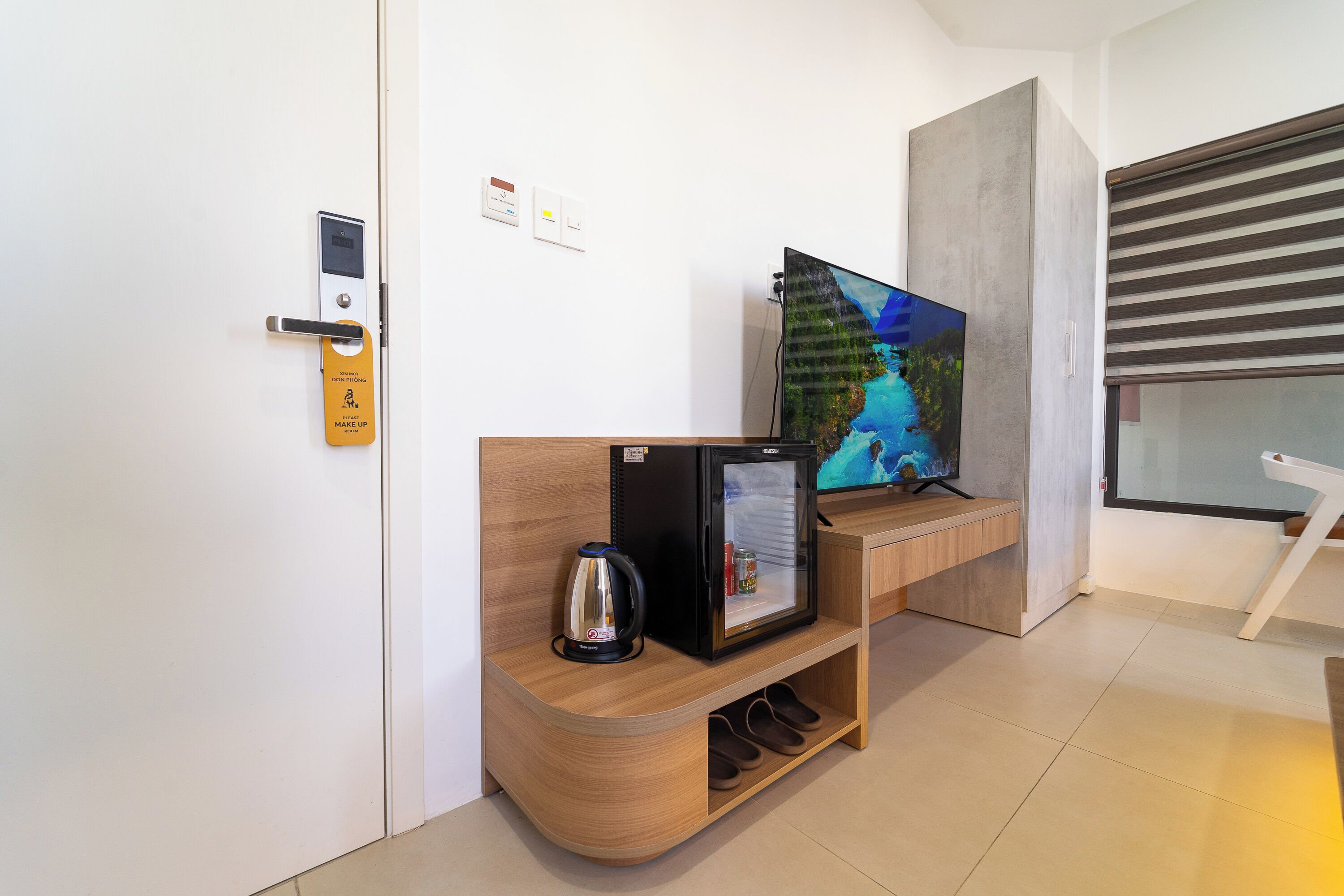 Moderni hotellihuone, jossa on puinen vastaanottotiski, minibaari, televisio ja liukuovi.
