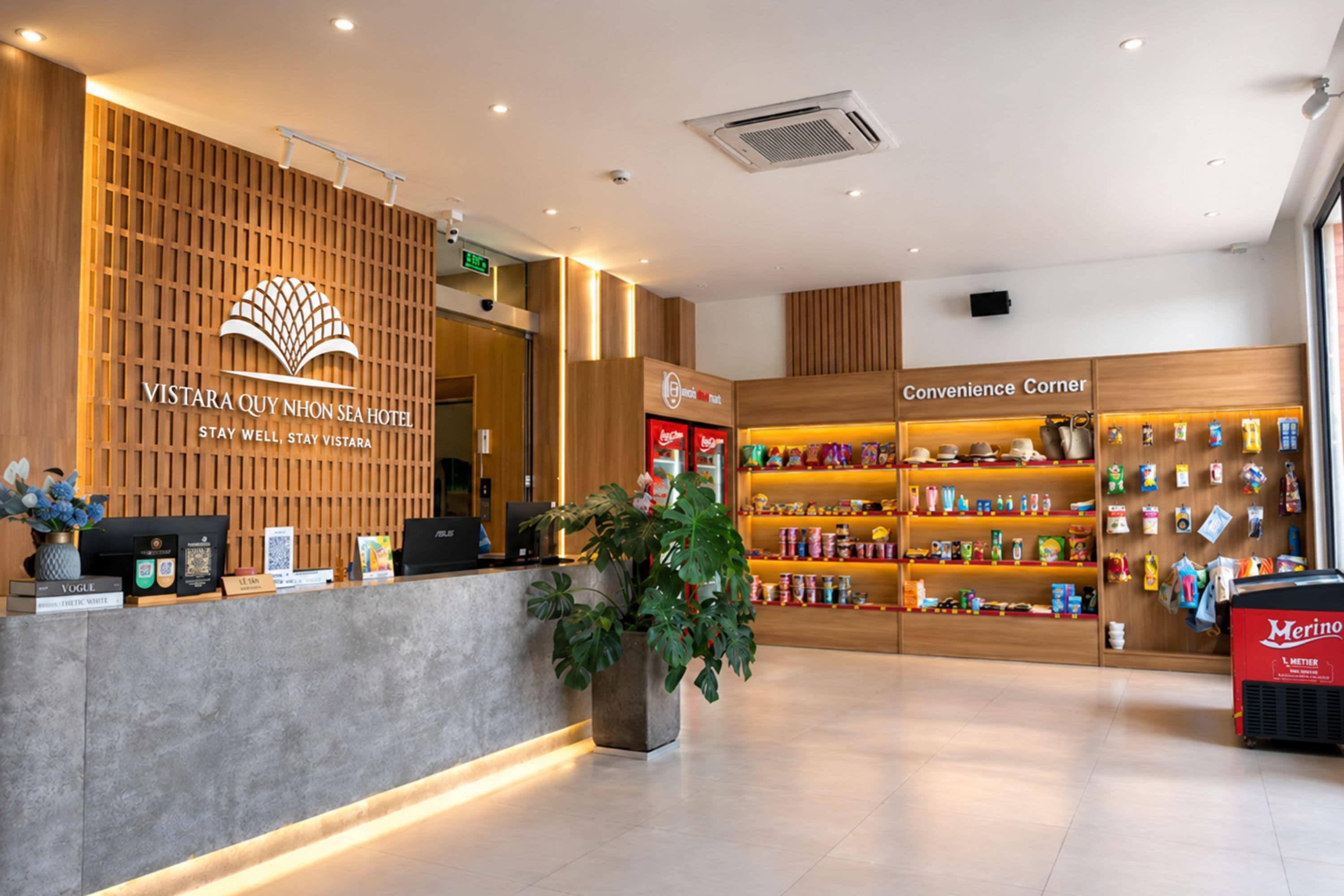 A hotel reception area with a wooden reception desk, a plant, and a convenience store.