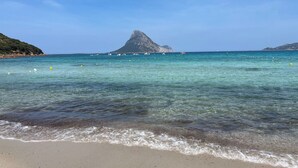 A beach with clear turquoise water, a prominent rocky hill in the background, and several boats. - Il Vecchio Faro 66 (Loiri Porto San Paolo)
