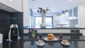 A modern kitchen with a coffee machine, a croissant, and two cups of coffee on the counter. - Il Vecchio Faro 66 (Loiri Porto San Paolo)