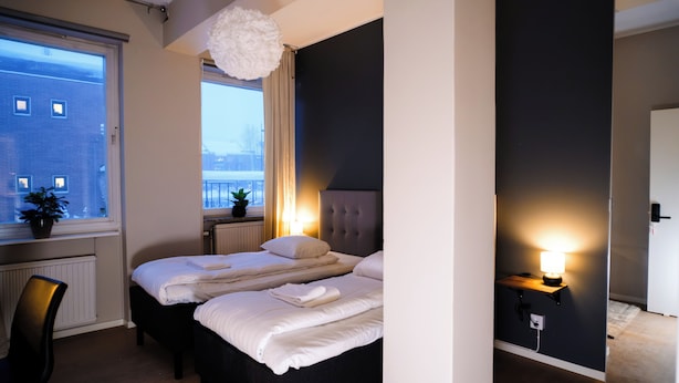 Une chambre moderne avec un grand lit, un bureau et une vue sur la ville par la fenêtre.