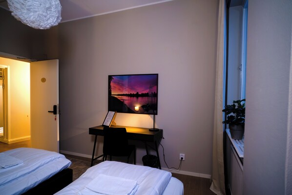 Un dormitorio con dos camas, un escritorio con una computadora, un cuadro en la pared y una ventana con vistas.
