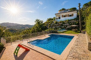 Ein rechteckiger Pool mit Steinbord, Metallgeländer und Blick auf ein Haus mit Balkon.