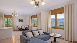 A living room with a grey sofa, a dining table with chairs, a chandelier, and large windows with curtains. - Spectacular views, just 4km to the beach! (Sant Cebrià de Vallalta)