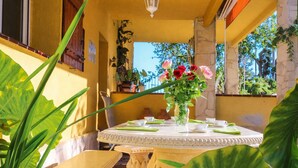 A round table with a vase of flowers, surrounded by chairs and a tablecloth, in a sunlit outdoor area with plants and a stone wall. - Spectacular views, just 4km to the beach! (Sant Cebrià de Vallalta)