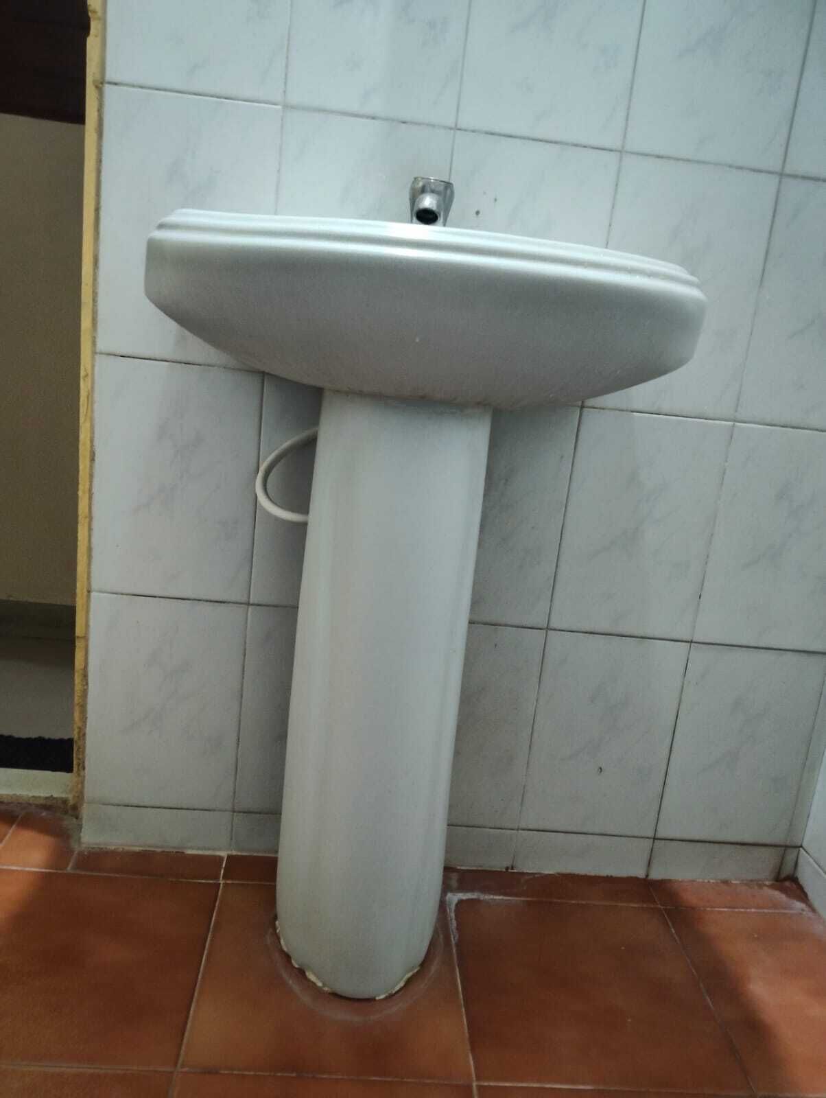 A bathroom with a pedestal sink, tiled walls, and terracotta floor tiles.
