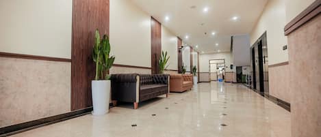 A spacious, well-lit hallway with a polished marble floor, a black and brown sofa, and potted plants.