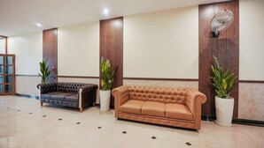 A lobby with two leather sofas, a wooden panel wall, and a standing fan. - KAYAL RESIDENCY (Gobichettipalayam)