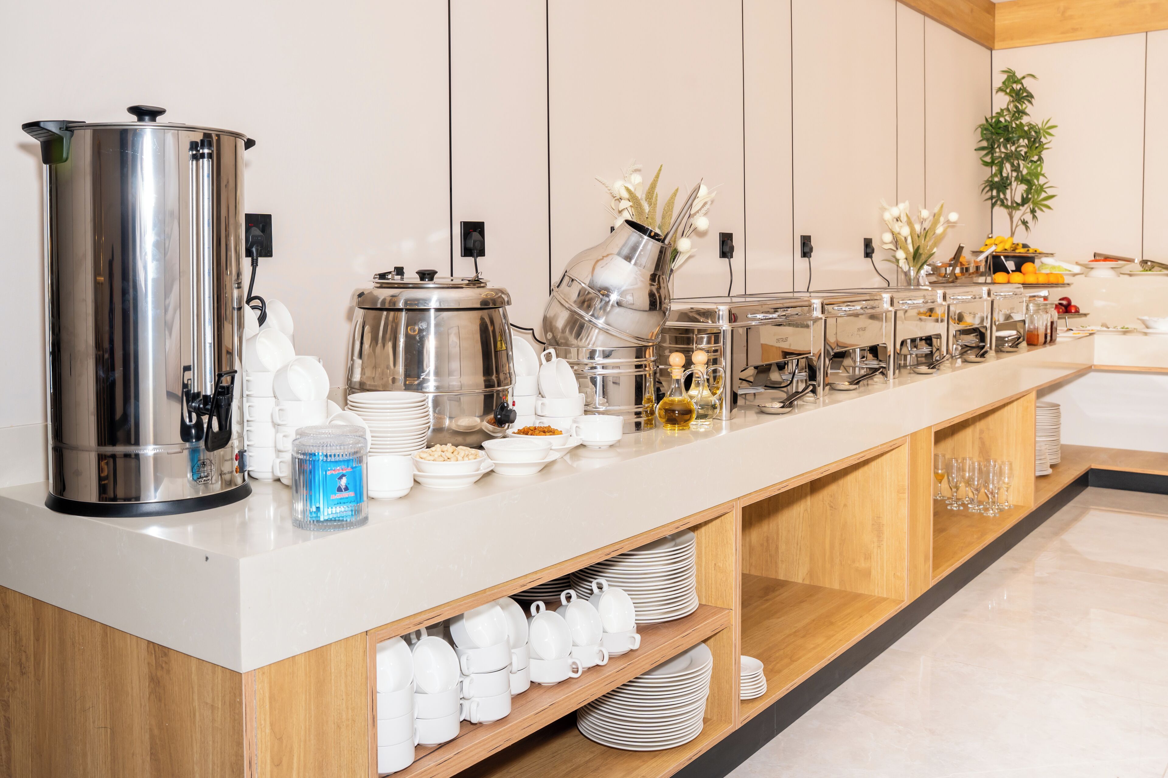 A buffet setup with a coffee station, various food containers, and a decorative vase with flowers.