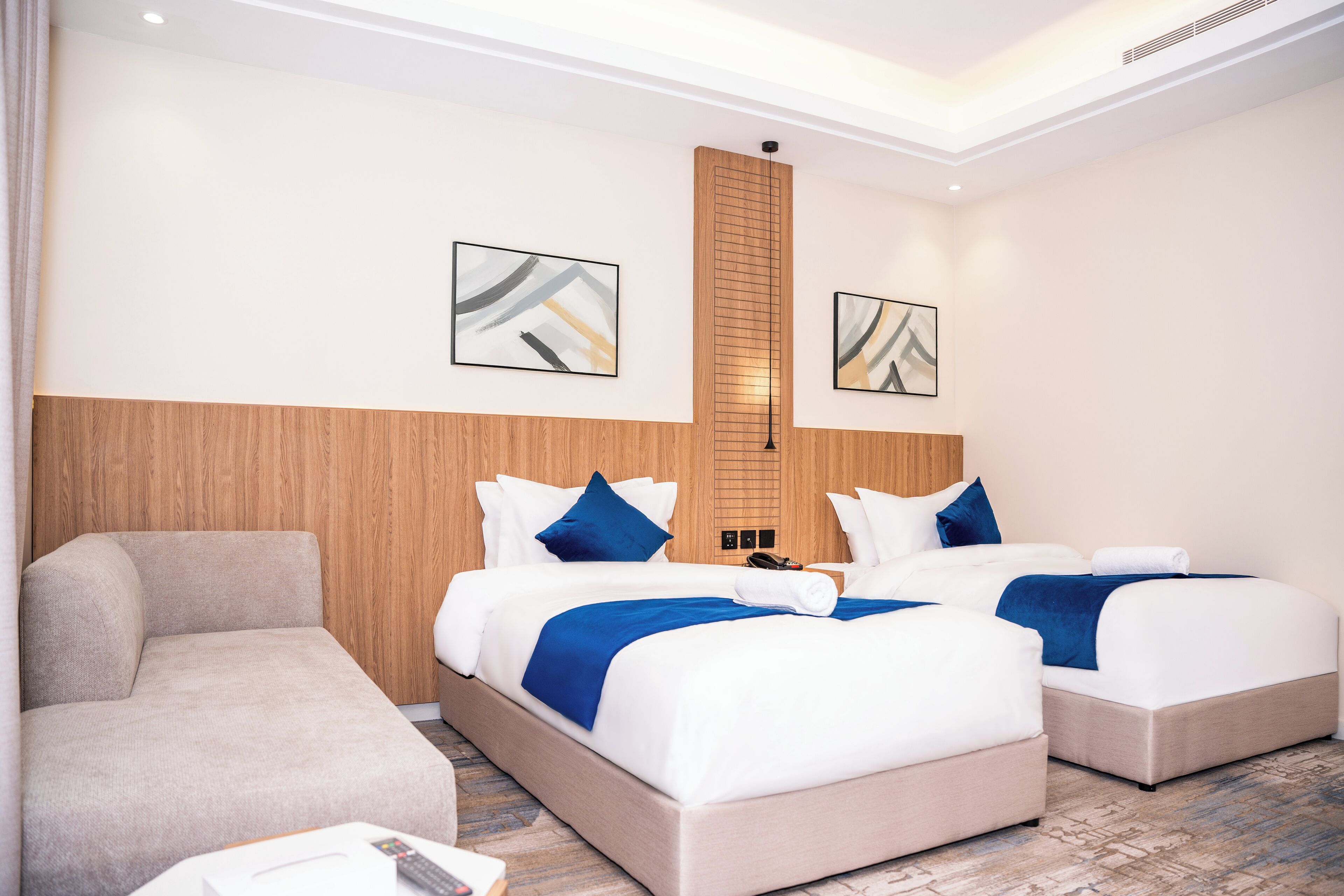 A hotel room with two beds, a sofa, and artwork on the walls.