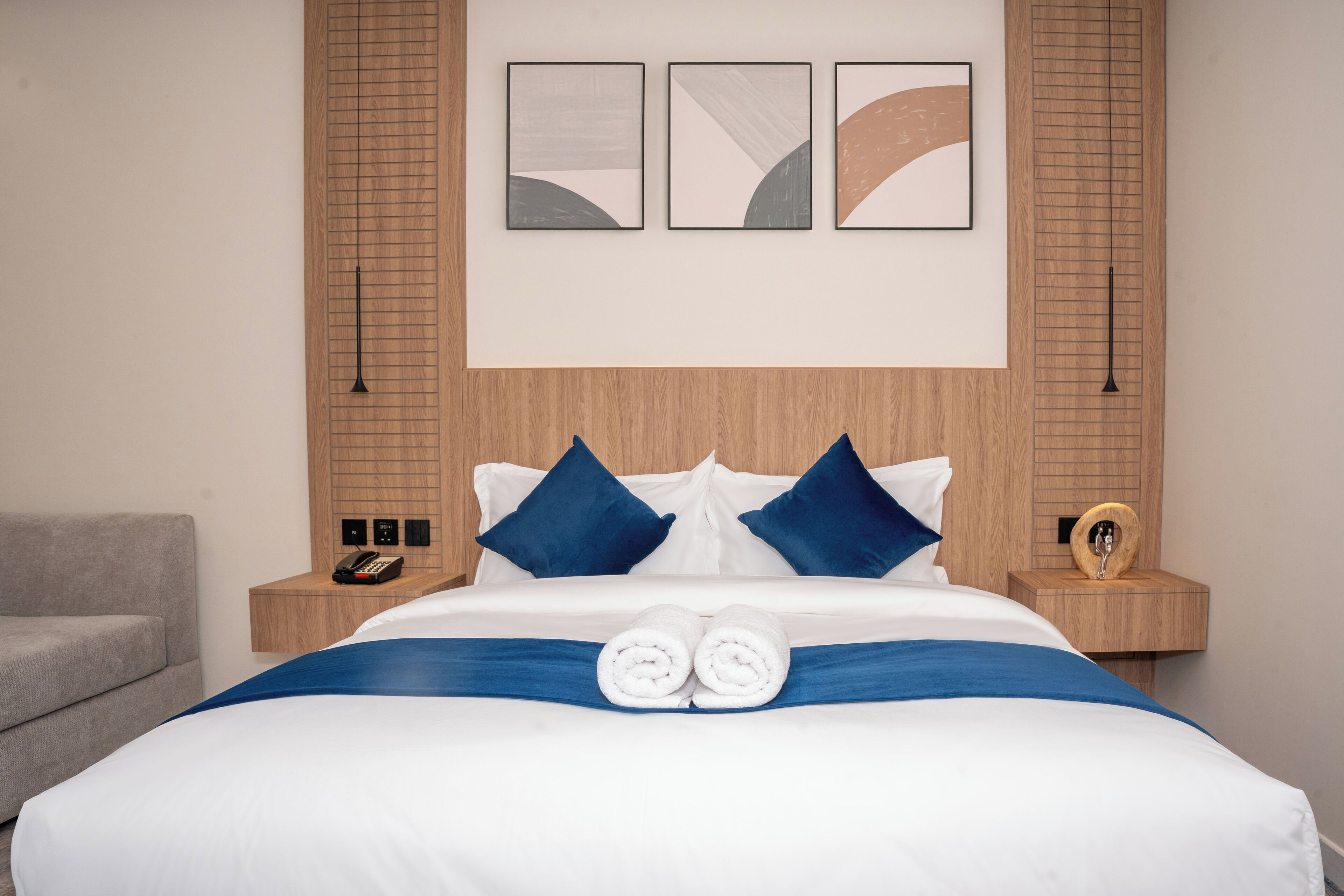 A neatly made bed with blue and white bedding, two pillows, and a blue accent strip. There are two bedside tables with a phone and a decorative item.