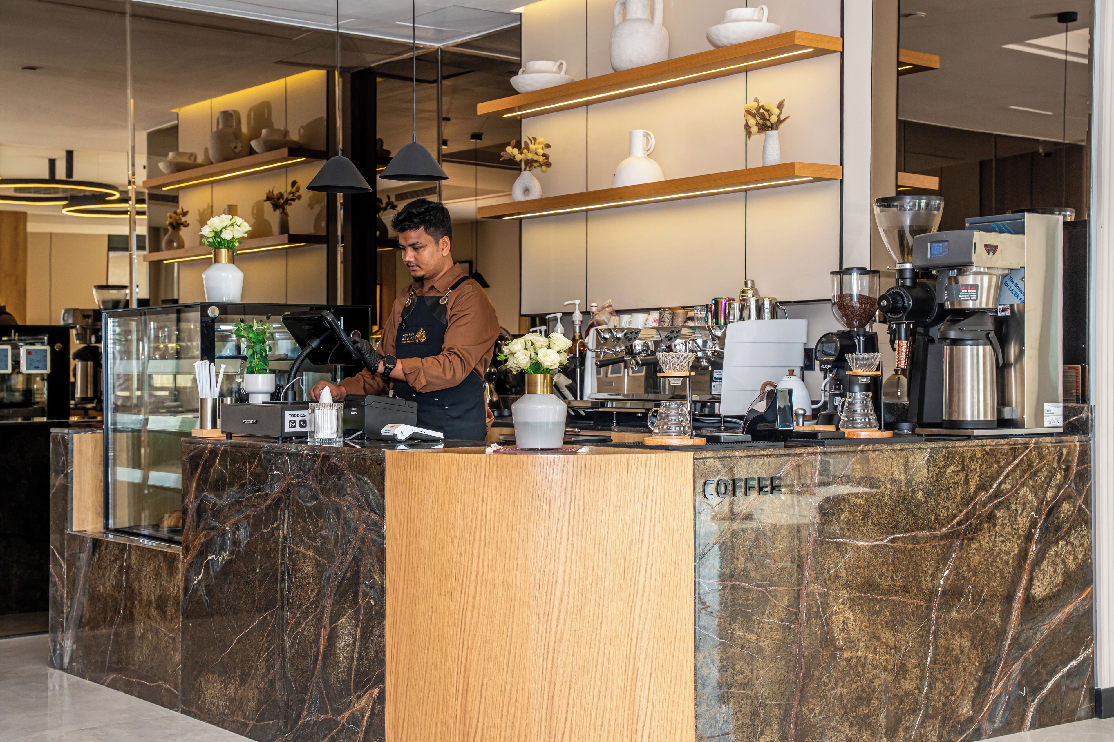 A modern coffee shop with marble countertops, a coffee machine, and shelves with decorative items.