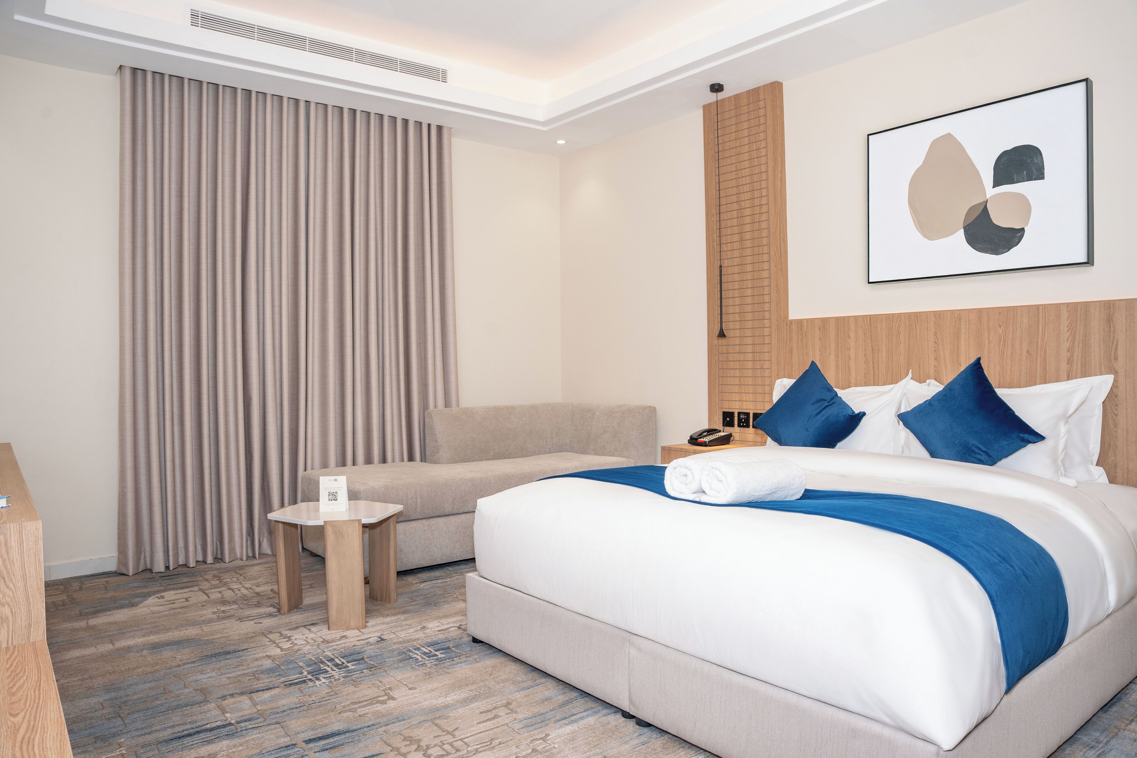 Une chambre d’hôtel avec un lit, un canapé, une petite table et une œuvre d’art accrochée au mur.