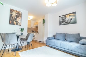 Un salon moderne avec un canapé gris, une table à manger avec des chaises et deux œuvres d’art représentant des éléphants, accrochées au mur.