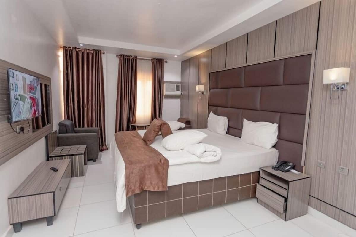 A modern hotel room with a large bed, a bedside table, a desk, and a chair.