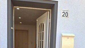 Une porte ouverte donne sur une pièce où se trouve un tapis à motifs, un interrupteur sur le mur et un panneau indiquant le numéro « 20 ».