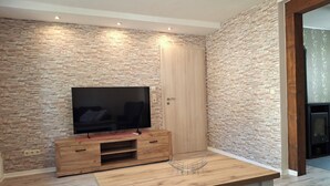 Un salon moderne avec un téléviseur à écran plat posé sur un meuble en bois, une table en bois et un mur à la texture pierre.