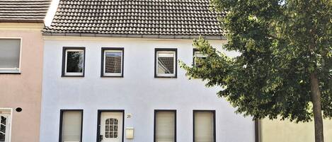 A two-story building with a tiled roof, a white facade, and a black base. There are four windows on the second floor and a door with a glass panel.