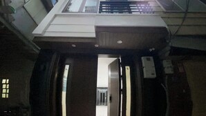 An interior view of a building with a central elevator shaft, tiled floors, and a visible door leading to another area. - GAIA House Le Duan (Hanoi)