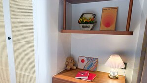 A compact room with a wooden desk, a small shelf with decorative items, a teddy bear, and a lamp. - GAIA House Le Duan (Hanoi)
