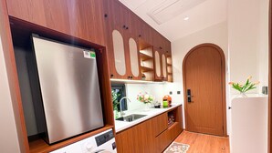 A compact kitchen with a built-in washing machine, a refrigerator, and wooden cabinets. - GAIA House Le Duan (Hanoi)
