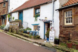 A white building with a blue door and window shutters, a small table outside, and a signboard for Harbour Gallery and Tea Room. - Seascape Cottage at Crail Harbour (Crail)