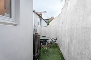 A narrow courtyard with a table and chairs, a small garden area, and a white wall. - Seascape Cottage at Crail Harbour (Crail)