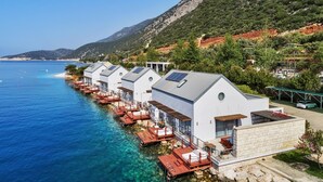 A row of white seaside cottages with clear blue waters and a mountainous backdrop. - Doria Hotel&Yacht Club (Kaş)