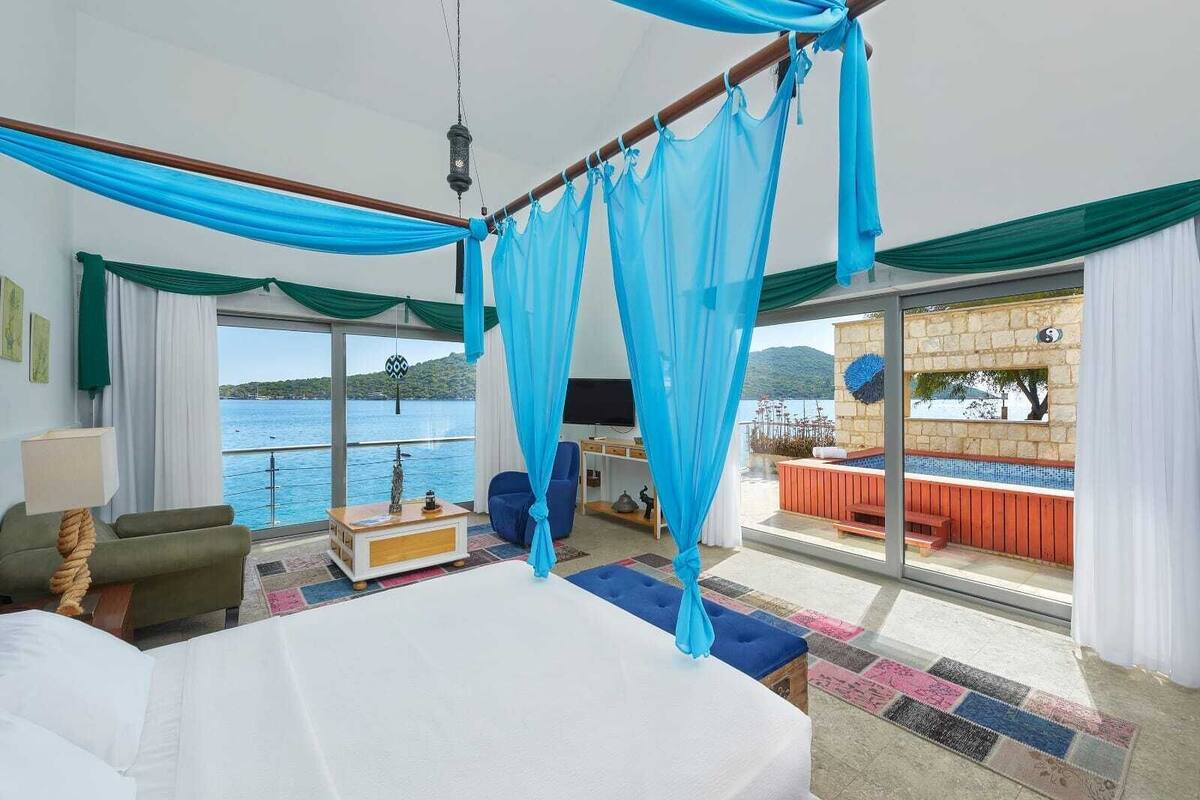 A bedroom with a large bed, a TV, and a view of the sea.